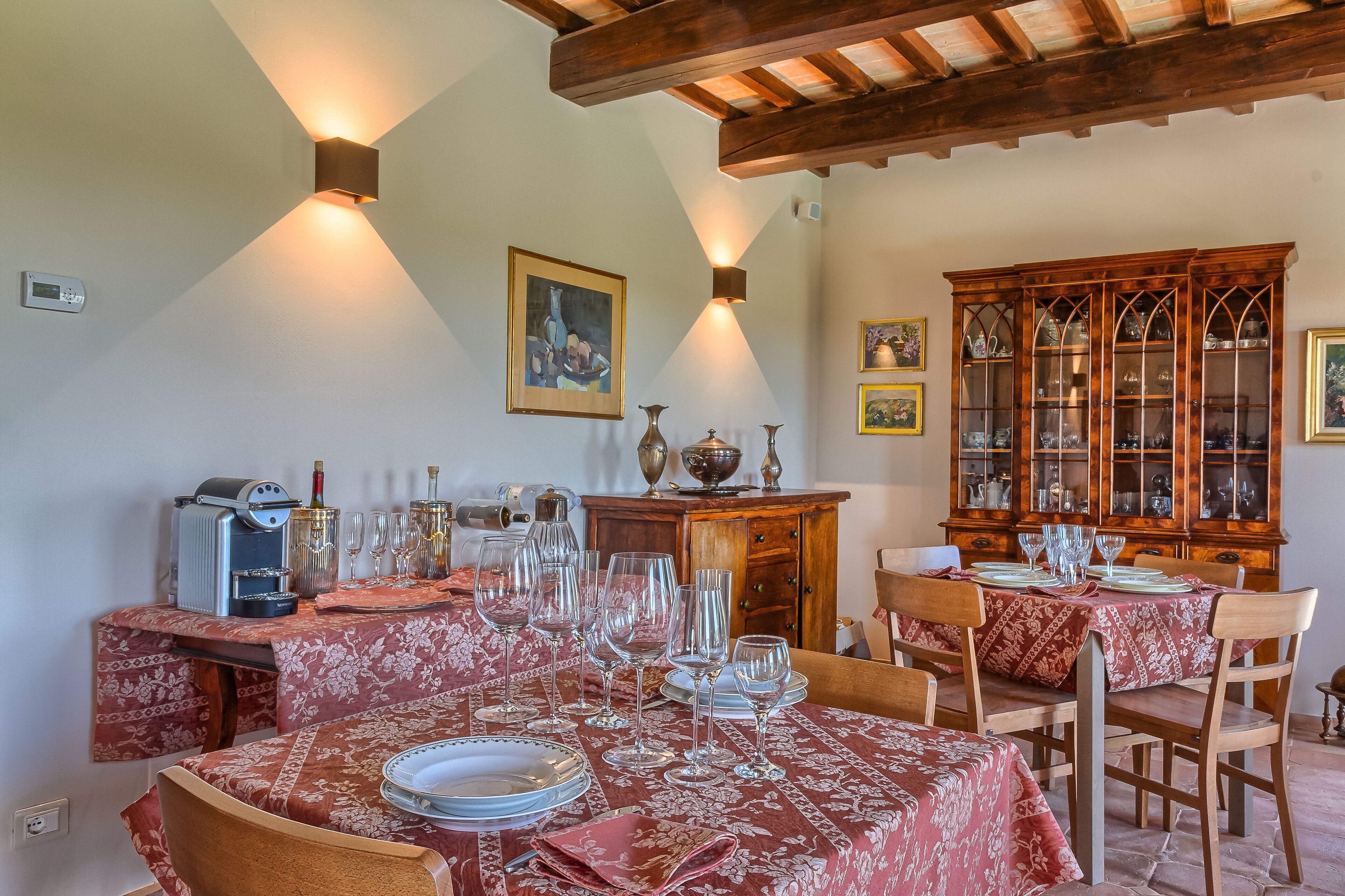 A dining area with tables set for a meal, a coffee machine, and a cabinet with glassware.