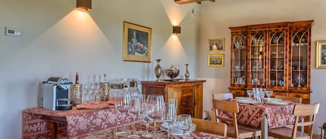 A dining area with tables set for a meal, a coffee machine, and a cabinet with glassware.