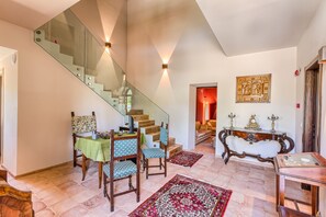 Una escalera con barandillas de vidrio, un comedor con sillas estampadas, una mesa consola de madera y una alfombra roja con diseño.