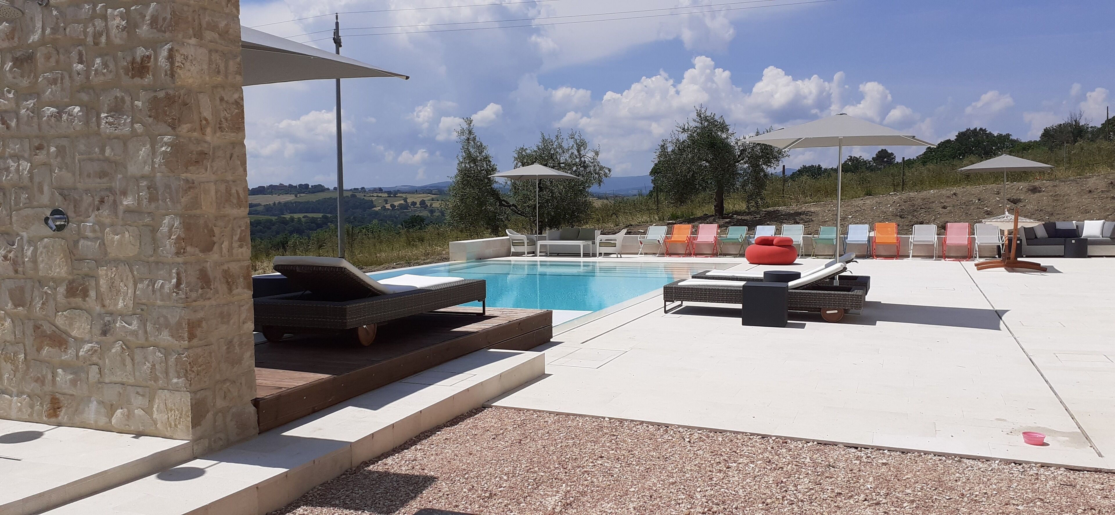 Zona de piscina amb gandules i ombrelles, envoltada de murs de pedra i vistes al camp.