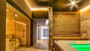 Un moderno espacio de spa con sauna de vidrio, pared de madera e hidromasaje iluminado en verde.