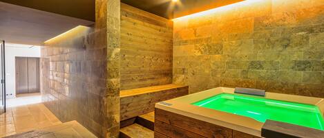 Une salle de bain moderne avec un meuble-lavabo en bois, une baignoire intégrée dotée d’un éclairage vert et un mur en pierre.