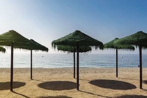 A beach with three thatched umbrellas and a sandy shore. - Villa Delfín Blanca with fantastic views and private pool (Salobreña)