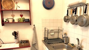 Una cocina con dos fregaderos, un escurreplatos, utensilios colgantes y un cesto de basura.