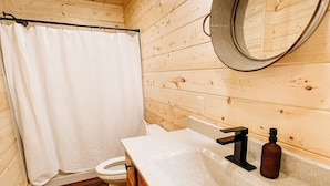 A wooden cabin bathroom with a toilet, sink, and shower curtain.