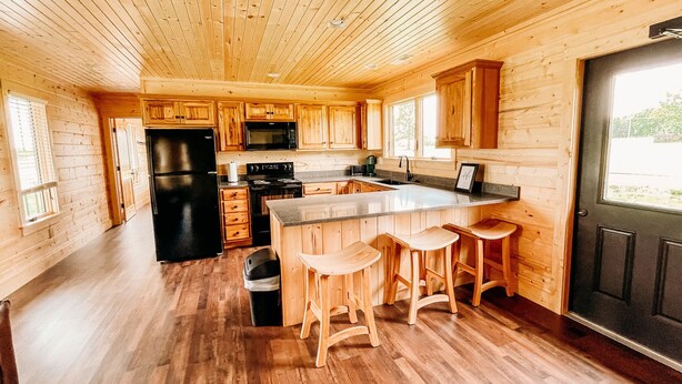 A spacious kitchen with wooden cabinets, a black refrigerator, a microwave, and a large island with bar stools.