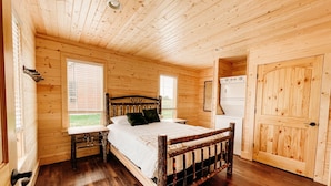 A wooden cabin bedroom with a bed, a nightstand, a dresser, and a door.