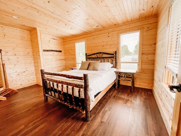 A wooden cabin bedroom with a bed, a nightstand, and a window.