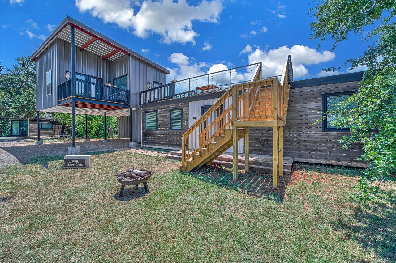 Une maison moderne à deux étages, dotée d’une terrasse en bois et d’un escalier menant à un balcon.