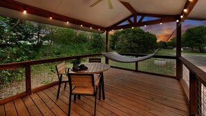 Eine Holzterrasse mit Tisch, Stühlen, einer Hängematte und einem Deckenventilator.