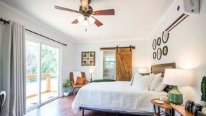Ein Schlafzimmer mit Bett, Stuhl, Schreibtisch, Deckenventilator und Blick ins Freie.