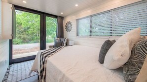 Een slaapkamer met een groot bed, een raam met zonwering, een decoratief wandobject en uitzicht op groen buiten.