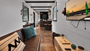 A narrow hallway with a wooden bench, a small table with a notebook, and a television mounted on the wall displaying a sunset bridge scene.