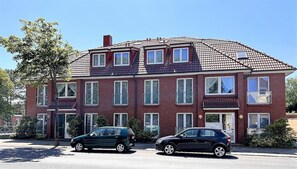 Un immeuble résidentiel de deux étages, doté d’une façade en briques rouges, de nombreuses fenêtres et d’un toit recouvert de tuiles.