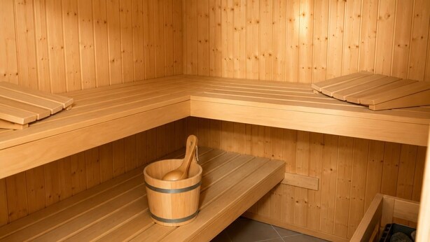 Una sauna con bancos de madera, un cubo de madera con una cuchara y un piso de baldosas.