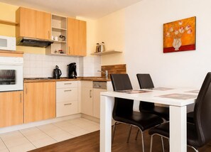 Ett modernt kök med träskåp, en vit bänkskiva, en inbyggd ugn, en kaffebryggare och en matplats med ett vitt bord och svarta stolar.