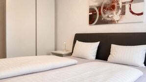 Una cama doble con sábanas blancas, una mesita de noche con lámpara y una obra de arte abstracto colgada en la pared.