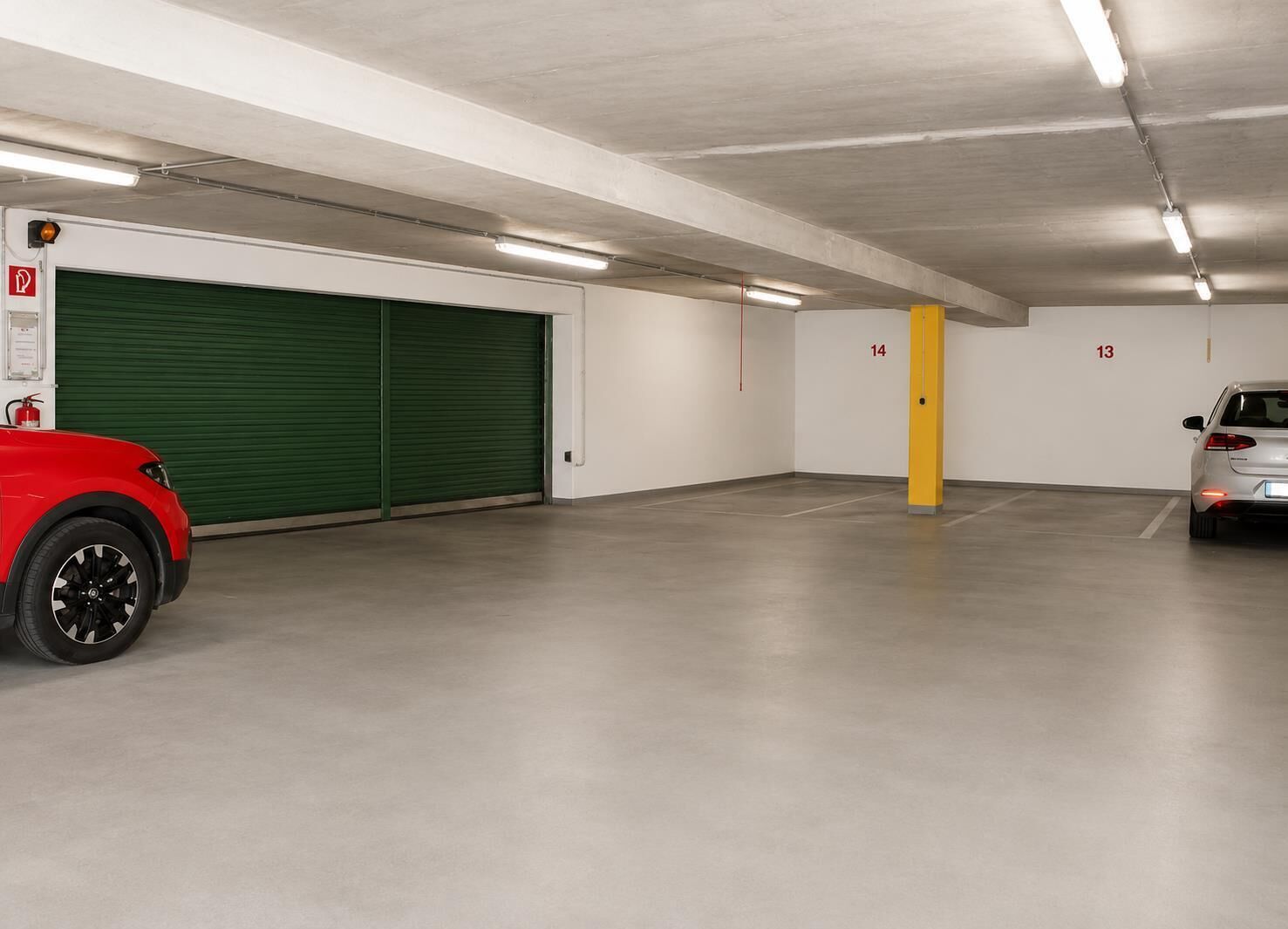 Un estacionamiento con puertas verdes, extintor y espacios numerados.