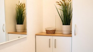 A bathroom with a mirror, two potted plants, a wicker basket, and a white cabinet with silver handles. - Haus am Mühlenpark Whg. 14, Steinmarnerstr.77/79, 27476 Cuxhaven (Cuxhaven- Döse)
