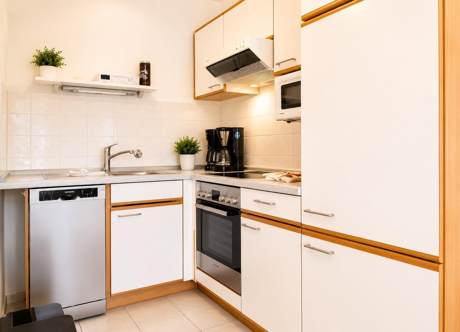 Une cuisine moderne avec des meubles blancs, un lave-vaisselle, une cuisinière et une machine à café.