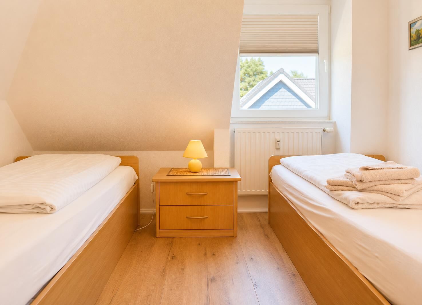 A bedroom with two single beds, a bedside table with a lamp, and a window with a view of a house.