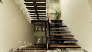 Una escalera moderna con detalles de madera y barandilla metálica, que conduce a un rellano con una planta en maceta.