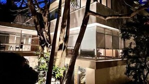 Un edificio moderno con ventanas amplias y un balcón, rodeado de árboles y plantas.