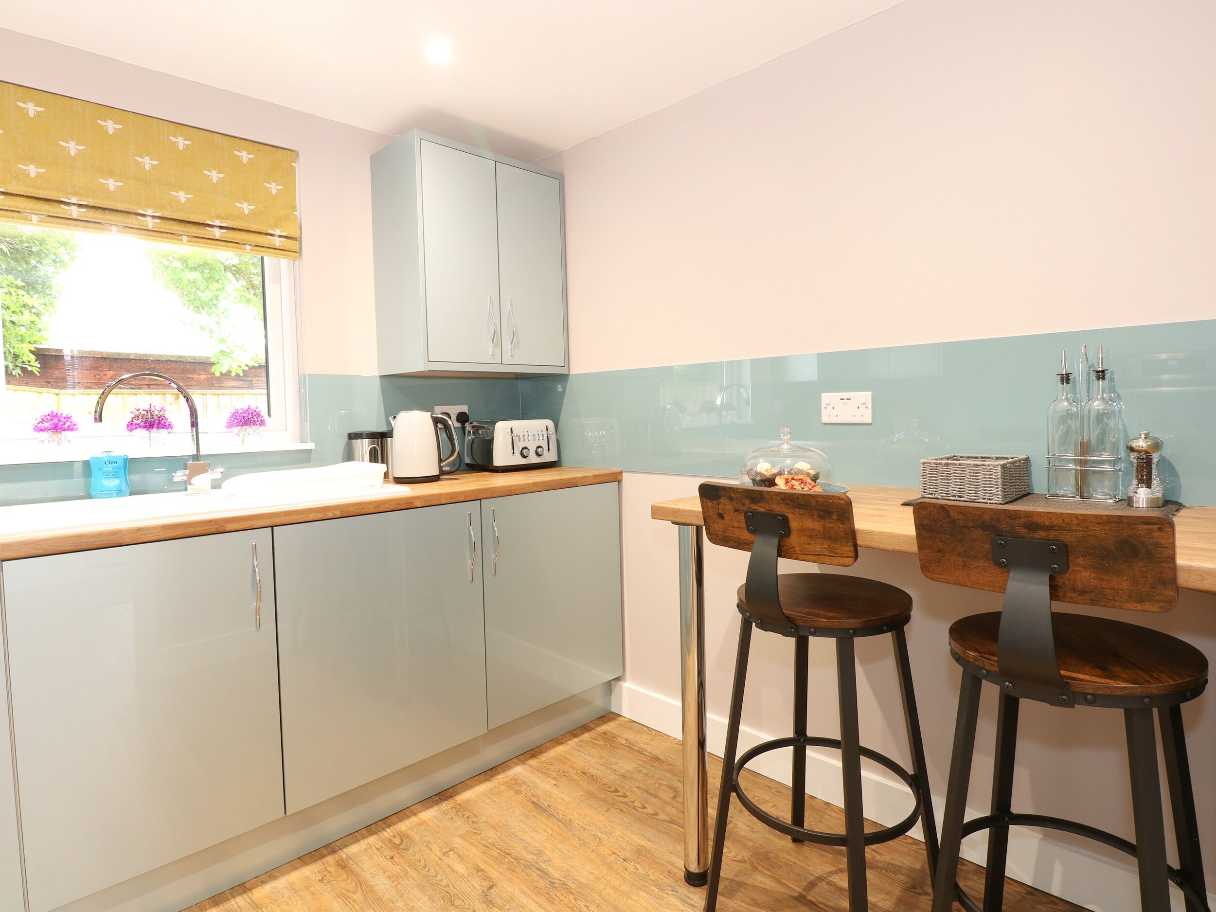 A kitchen with a wooden countertop, a sink, a kettle, a toaster, and two bar stools.
