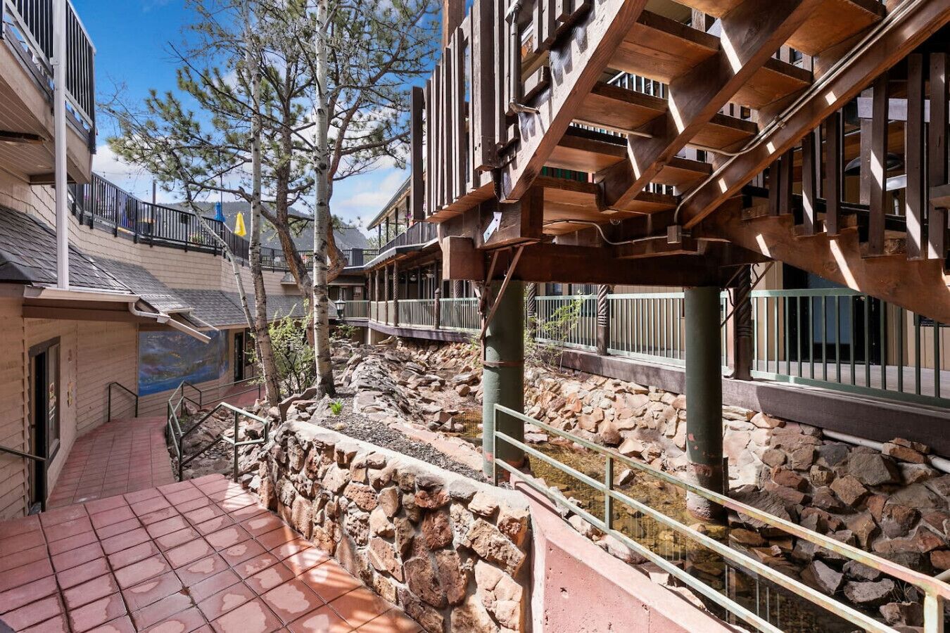 A courtyard with a stone wall, a wooden pergola, and a view of a building with a balcony.