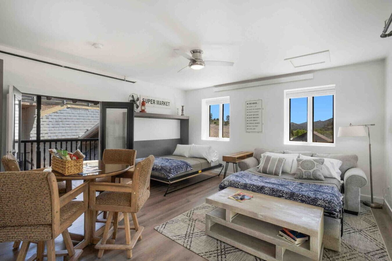 A modern, well-lit room with a bed, two sofas, a dining table, and a small kitchen area.