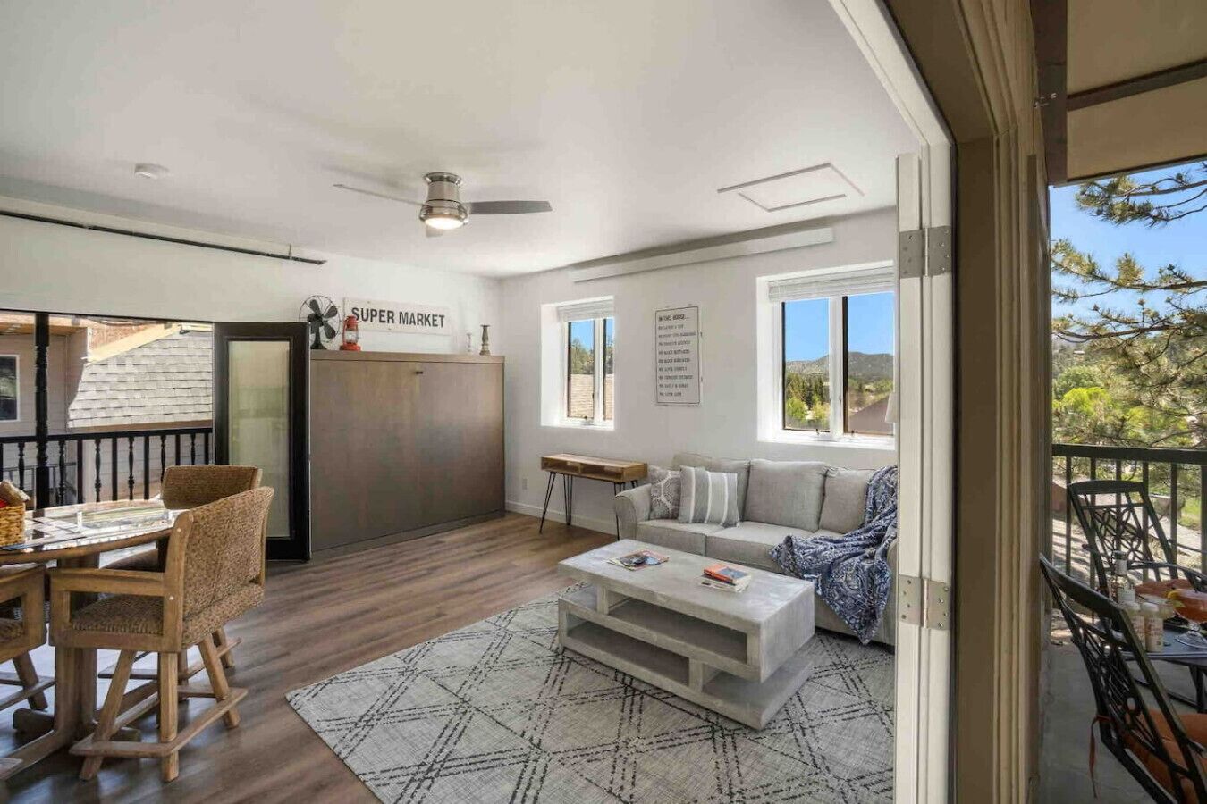Un grand espace de vie comprenant un canapé, une table basse et une table à manger. On peut voir un ventilateur de plafond et une enseigne indiquant « SUPERMARCHÉ ».