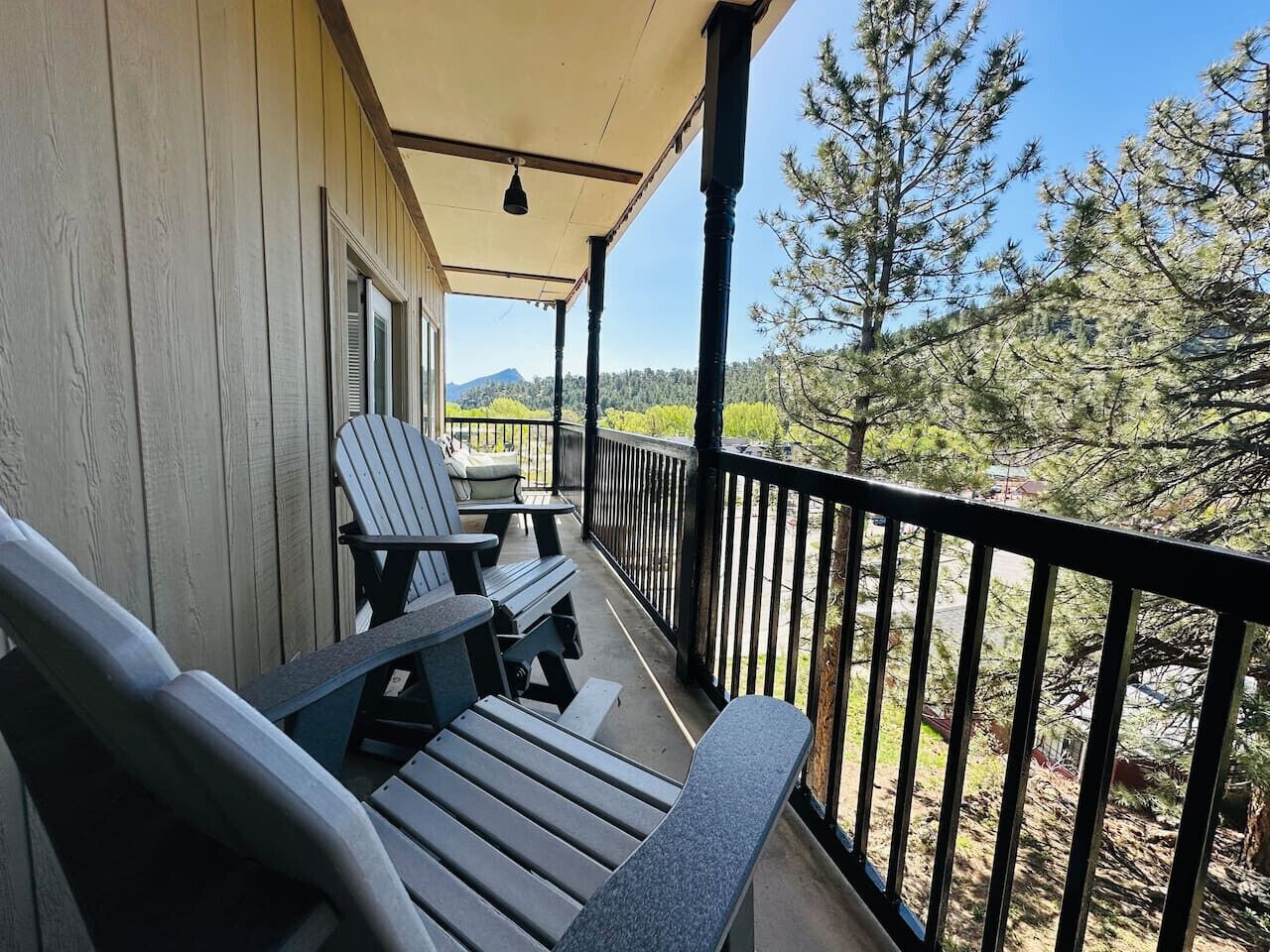 A wooden deck with Adirondack chairs and a table, overlooking a forested area.
