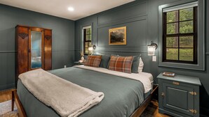 Un dormitorio con una cama grande, un armario de madera, una mesita de noche, una lámpara de pared y una ventana con vistas a zonas verdes.