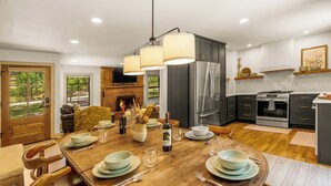 Una cocina moderna con comedor, que incluye una mesa de madera grande, armarios oscuros, electrodomésticos de acero inoxidable y una chimenea.