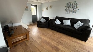 A living room with a black sofa, a wooden coffee table, and a television on a stand. - Barn conversion overlooking the golf course to the sea (Bude)