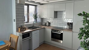 A modern kitchen with white cabinets, a built-in oven, a microwave, and a sink. - Barn conversion overlooking the golf course to the sea (Bude)