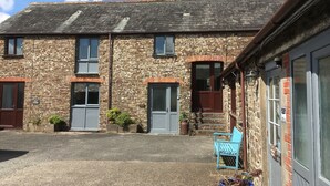 A stone building with a tiled roof, multiple doors, and windows. - Barn conversion overlooking the golf course to the sea (Bude)