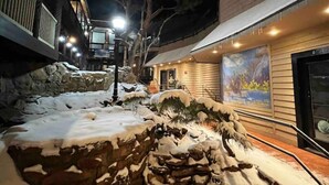 Ett snötäckt utomhusområde med stentrappor som leder upp till en byggnad med ett stort fönster där en färgstark väggmålning syns.