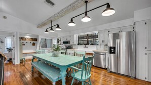 Una cocina amplia con suelo de madera, una mesa de comedor color turquesa y electrodomésticos de acero inoxidable.