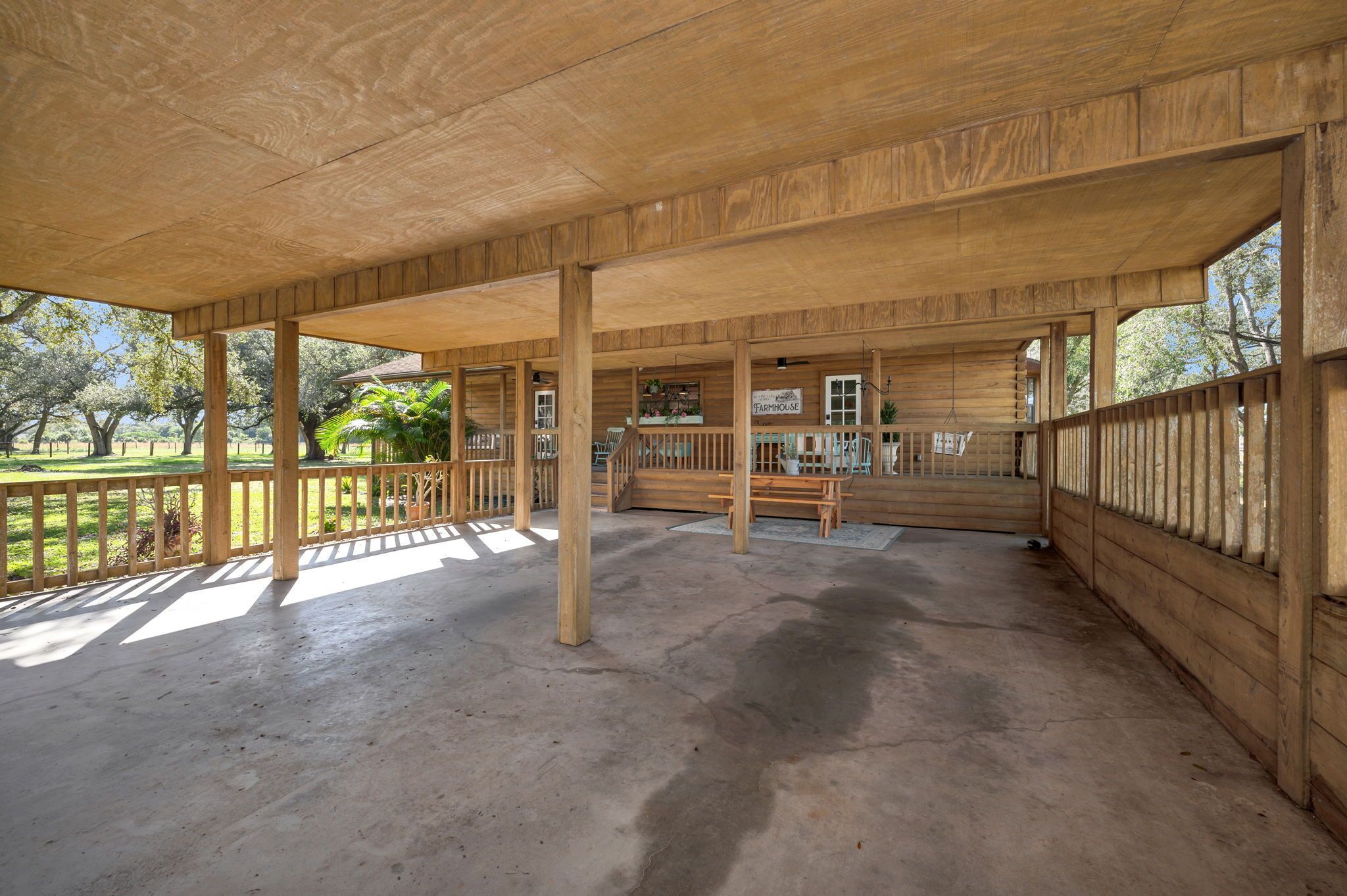 A covered wooden structure with a concrete floor, wooden railings, and a sign indicating a farmhouse.