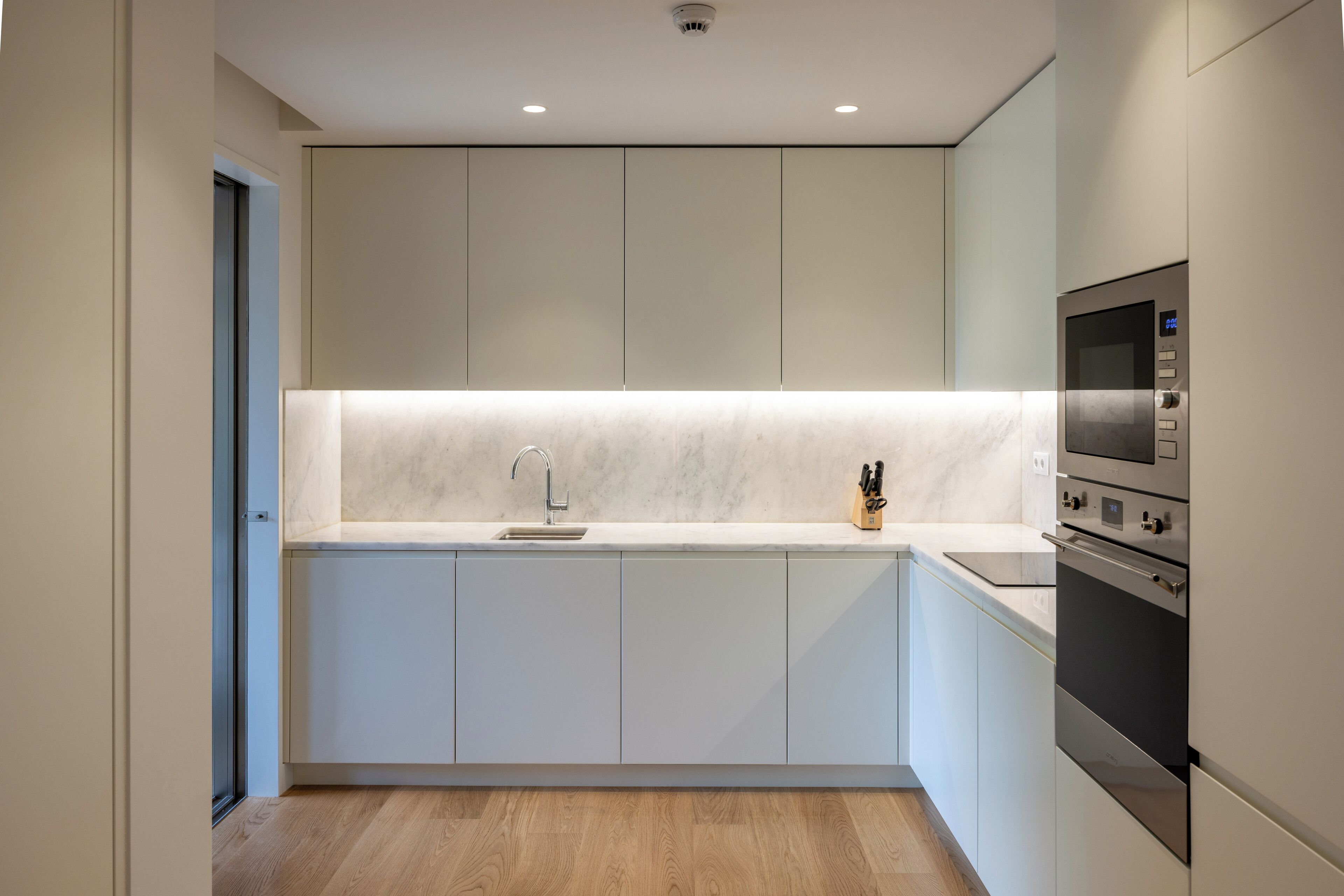 A modern kitchen with white cabinets, a marble countertop, a sink, and built-in appliances including an oven and microwave.