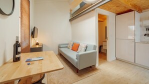 A modern kitchen with white cabinets, a dining area with a wooden table, and a light blue sofa with colorful cushions. - Mezzanine Stylish Apartment Q by Vacationy (Porto)
