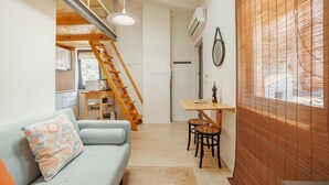 A compact living space with a sofa, a dining table with chairs, a wooden ladder, and a staircase leading to an upper level. - Mezzanine Stylish Apartment Q by Vacationy (Porto)