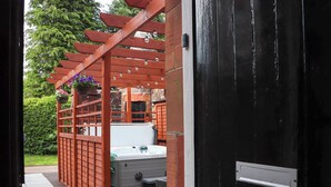 A wooden pergola with hanging flower baskets, a hot tub, and a black door. - Rob Roy Apartment (Glasgow)