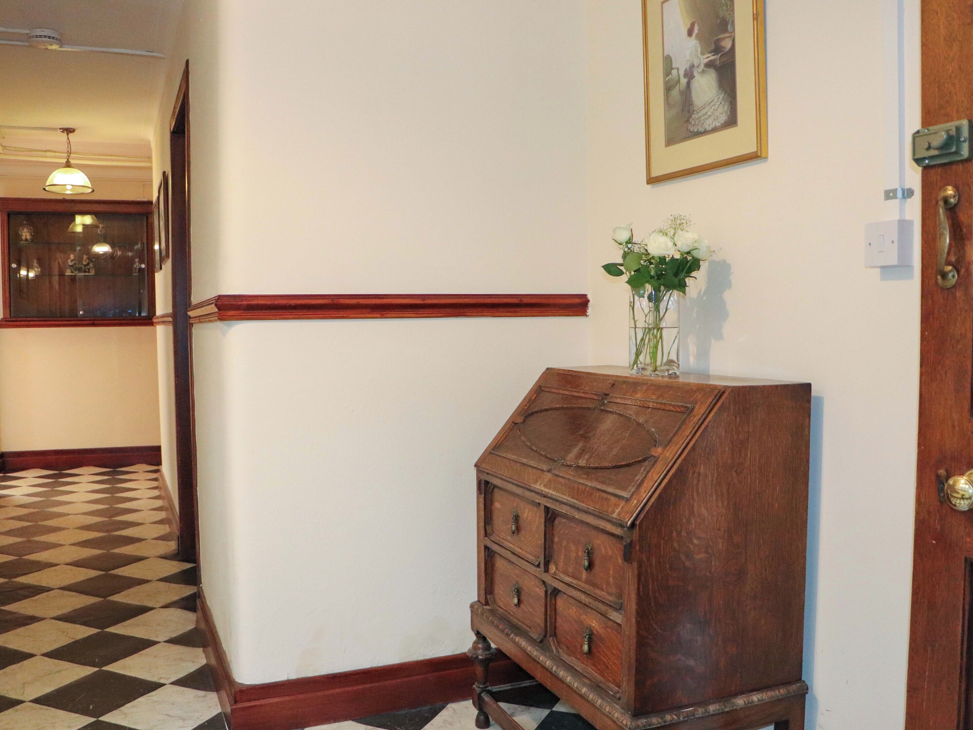 A hallway with a wooden cabinet, a checkered floor, and a framed picture on the wall.