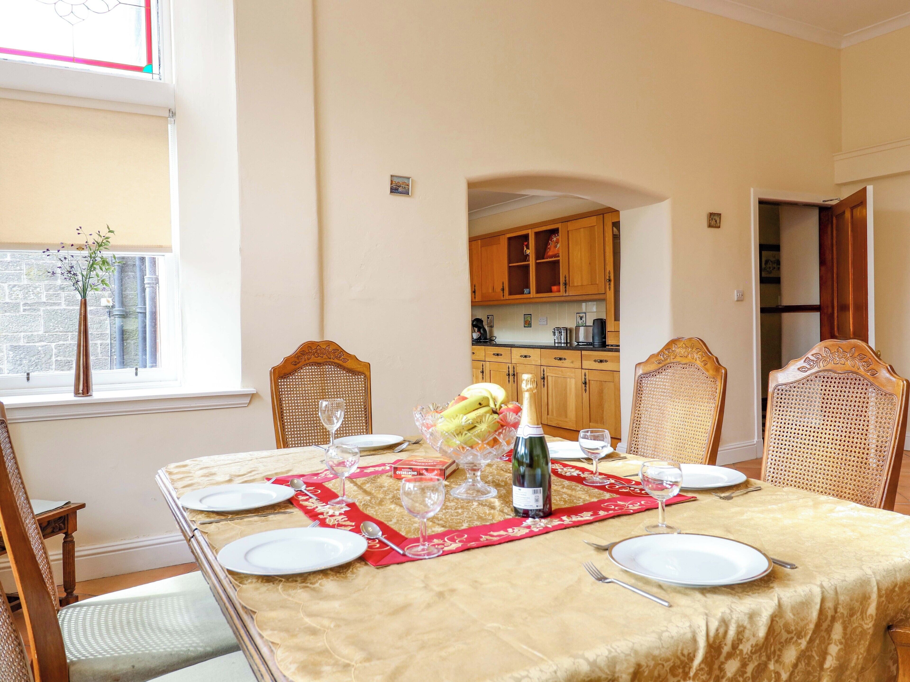 A dining room with a table set for four, featuring a red placemat, white plates, and a bottle of wine.