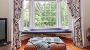A room with a bay window, a bench, and a television. - Rob Roy Apartment (Glasgow)