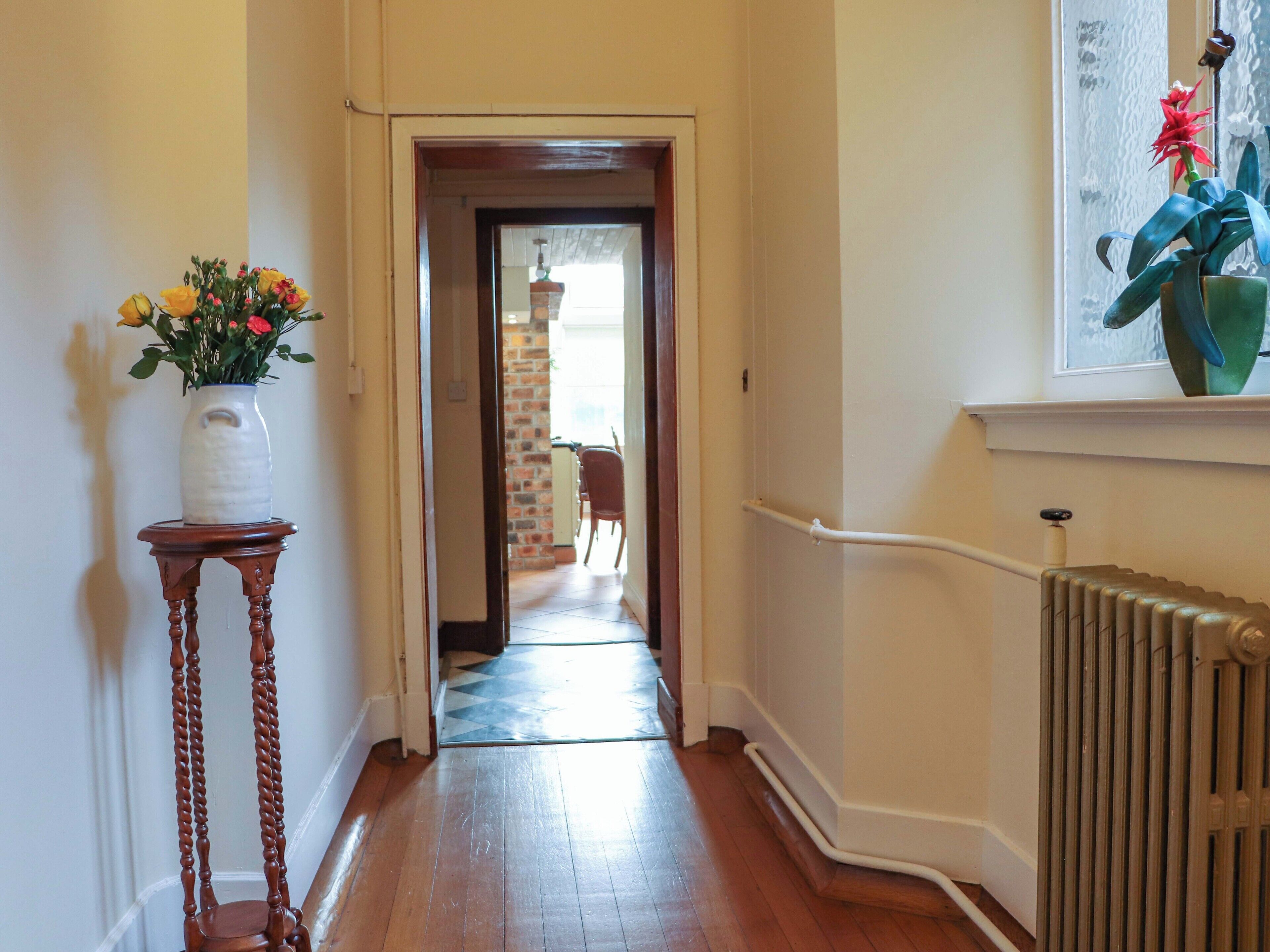A hallway with a wooden floor, a white vase with flowers, and a radiator.