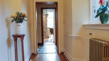 A hallway with a wooden floor, a white vase with flowers, and a radiator.