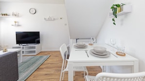 A modern, white-themed dining area with a TV, white chairs, and a dining table set for two. - Lovely 2-bed House in Kent - Parking Available (Greenhithe)